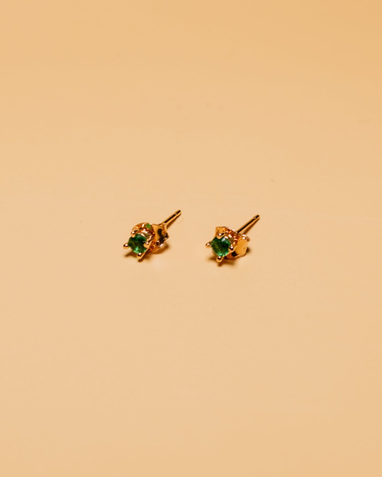 Gold earrings with green gemstones on a beige background