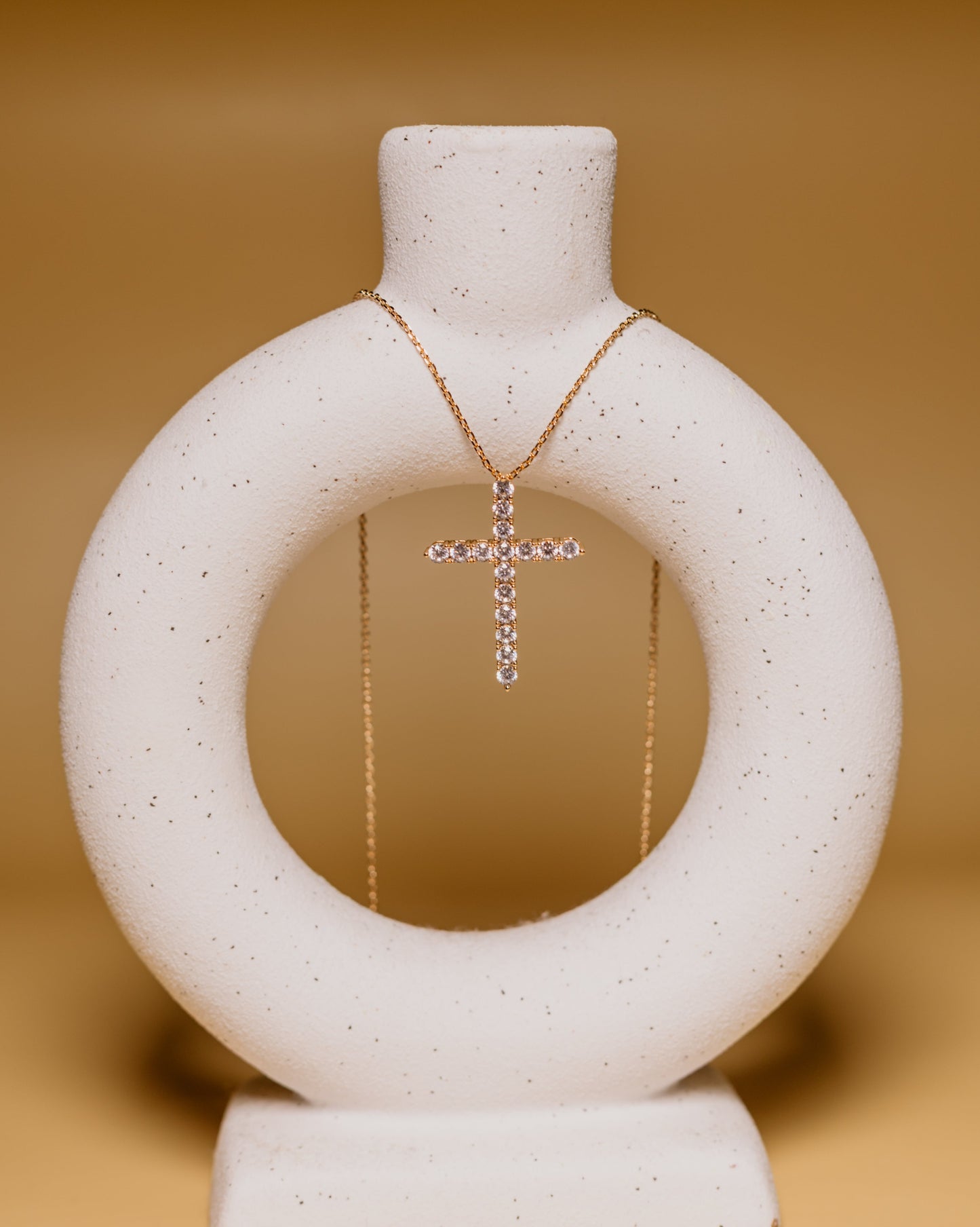 Necklace with a cross pendant on a white circular stand against a beige background