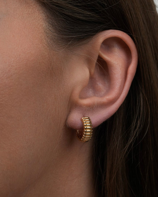 Close-up of gold plated small ribbed hoop earrings worn on ear