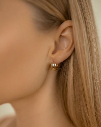 Close-up of a person wearing a gold earring with a neutral background