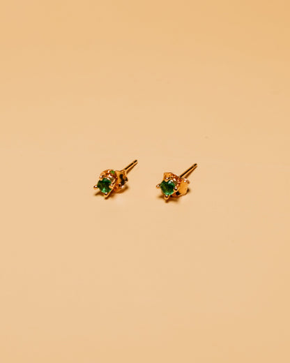 Gold earrings with green gemstones on a beige background