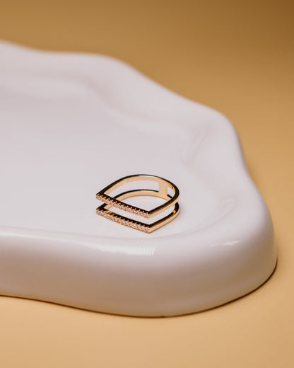 Close-up of a gold ring design on a white surface with a beige background