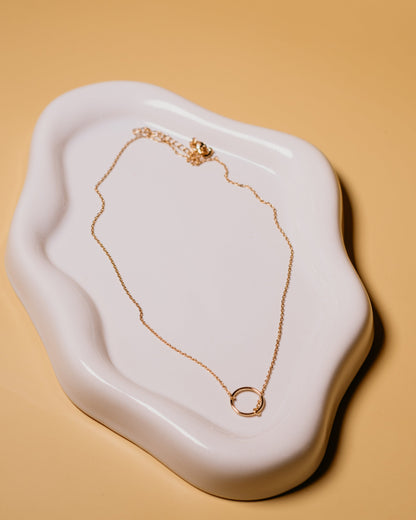 Gold necklace on a white dish with a beige background