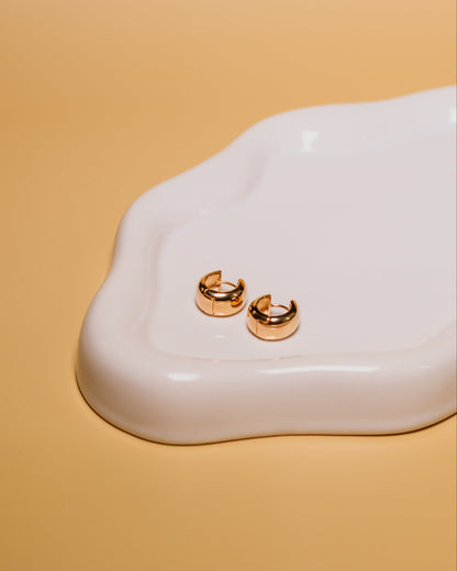 Gold hoop earrings on a white ceramic dish with a beige background