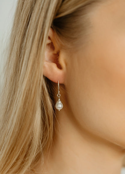 Pearl earring worn by a person with blonde hair, close-up shot.