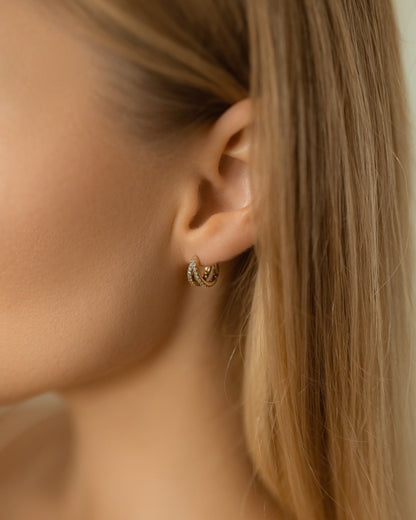 Close-up of a person wearing gold hoop earrings with a neutral background