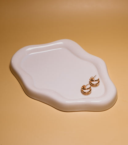 Gold hoop earrings on a white ceramic tray with a beige background