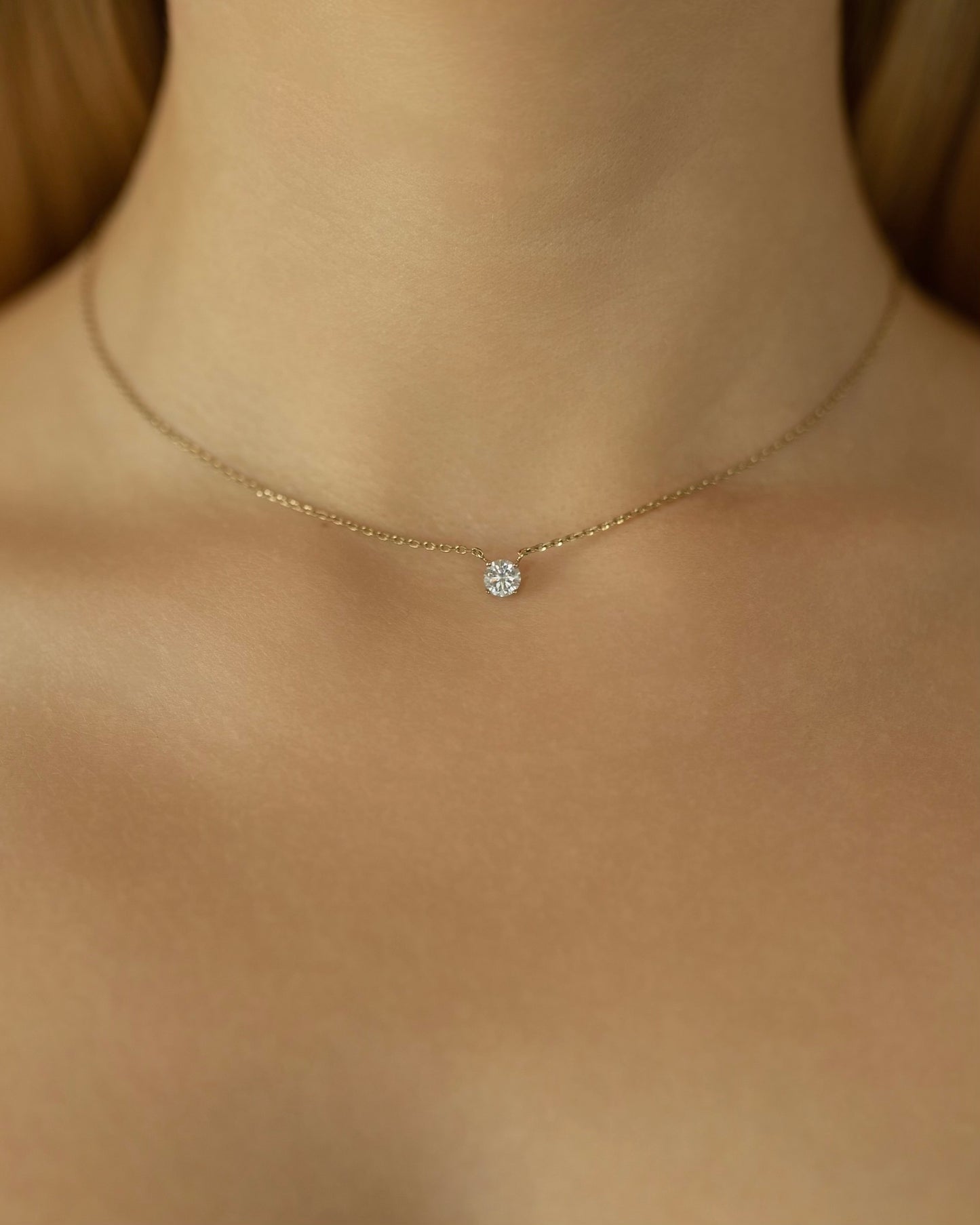 Gold necklace with a small round pendant on a person's neck