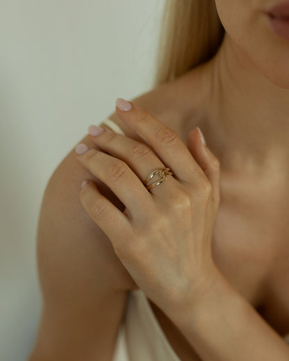 Close-up of a hand wearing a gold ring with a diamond, touching the shoulder against a neutral background.
