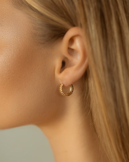 Close-up of a person wearing a gold hoop earring with a neutral background