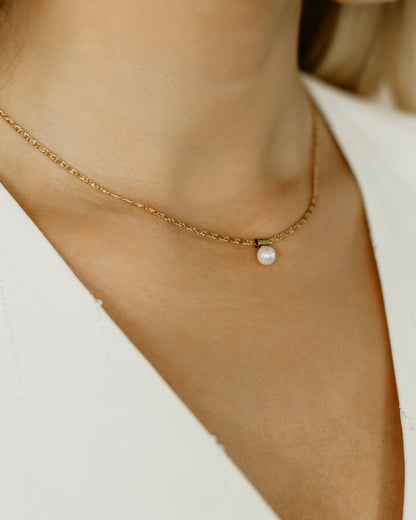 A person wearing a gold-filled chain necklace with a 6 mm shell pearl pendant.