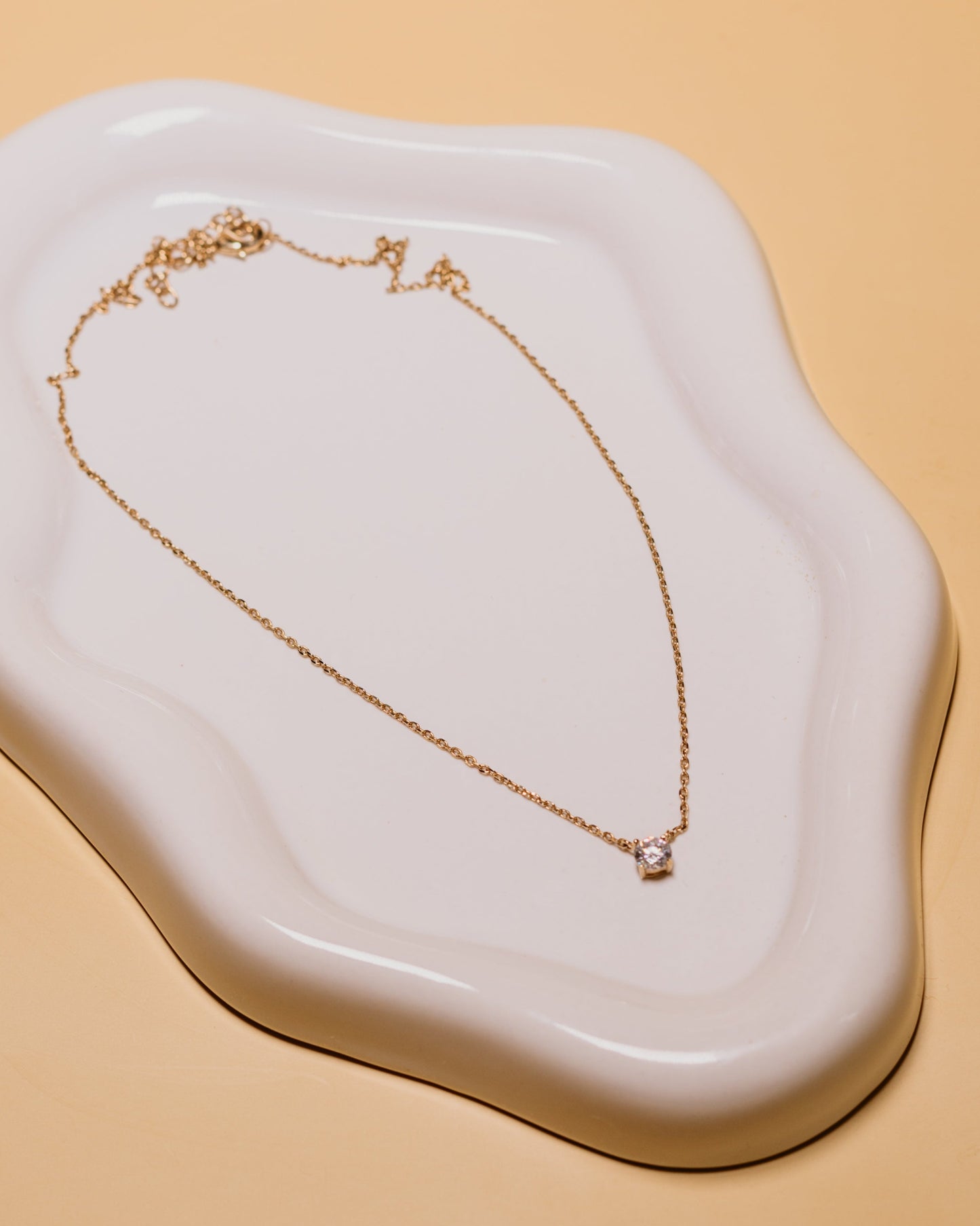 Gold necklace on a white ceramic dish with a beige background