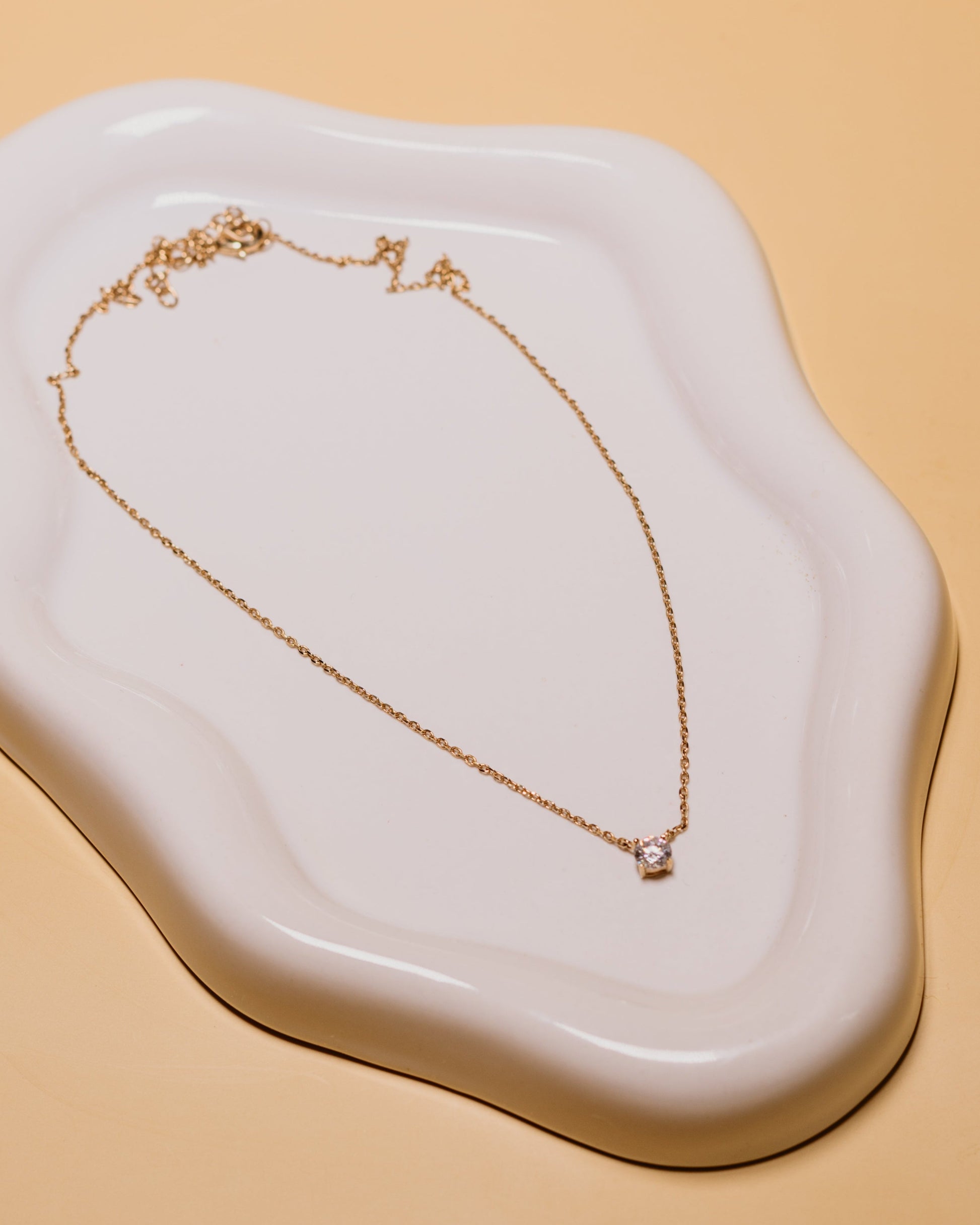 Gold necklace on a white ceramic dish with a beige background