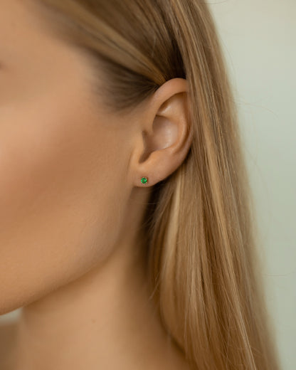 Close-up of an ear wearing a green earring with blonde hair.