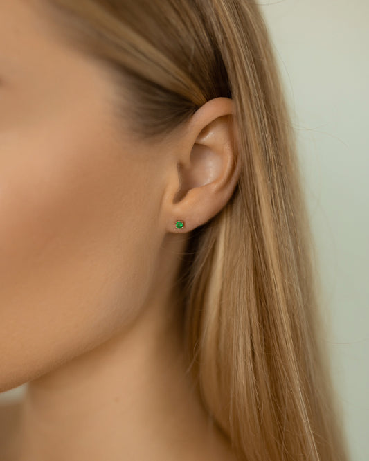 Close-up of an ear wearing a green earring with blonde hair.