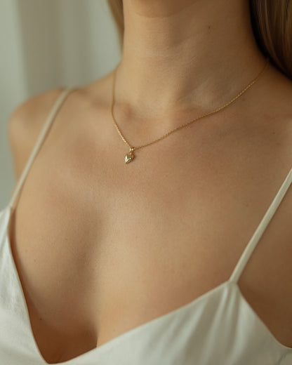 Gold necklace with a leaf pendant worn by a person in a white top.