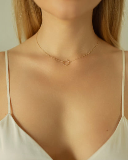Gold necklace on a person wearing a white top with a neutral background