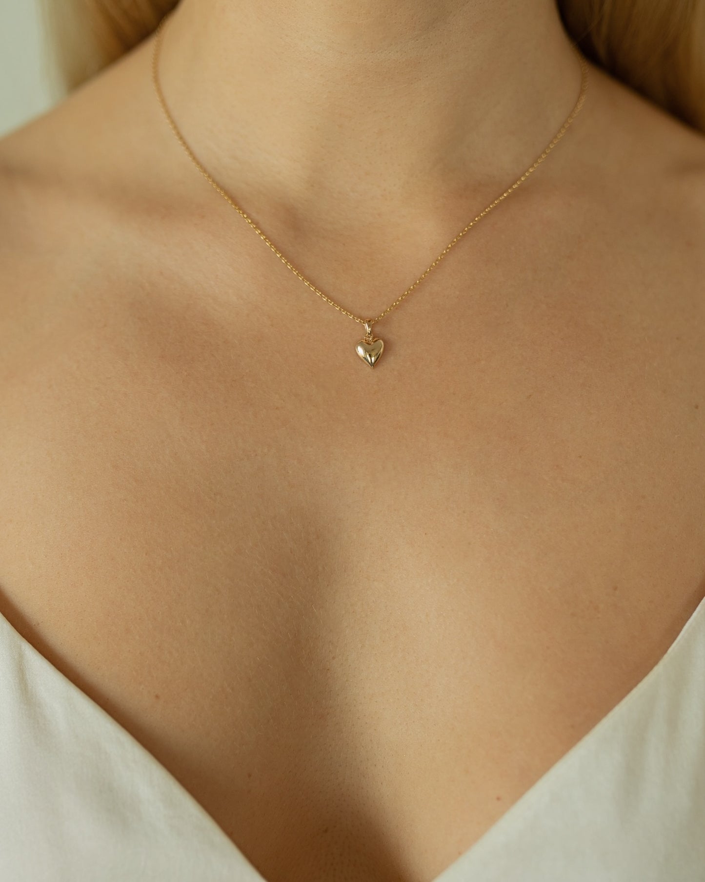 Gold necklace with a heart pendant on a person wearing a white top.