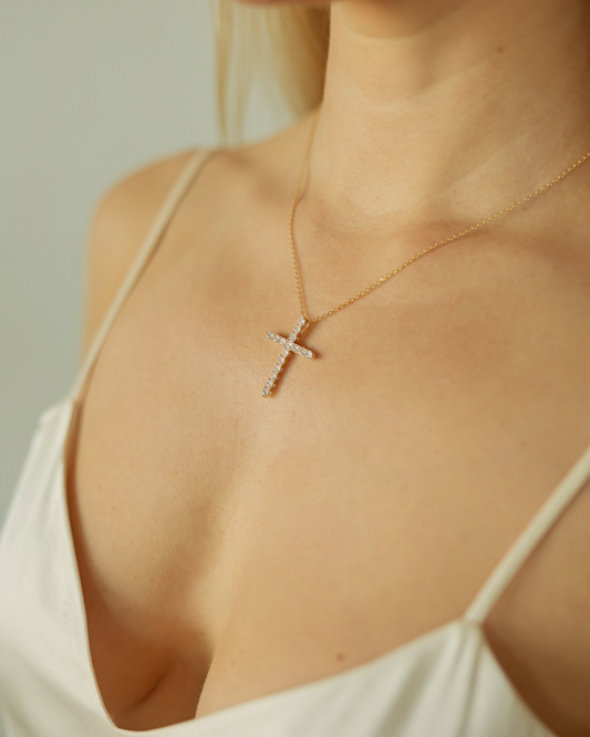 Gold cross necklace on a person wearing a white top against a neutral background