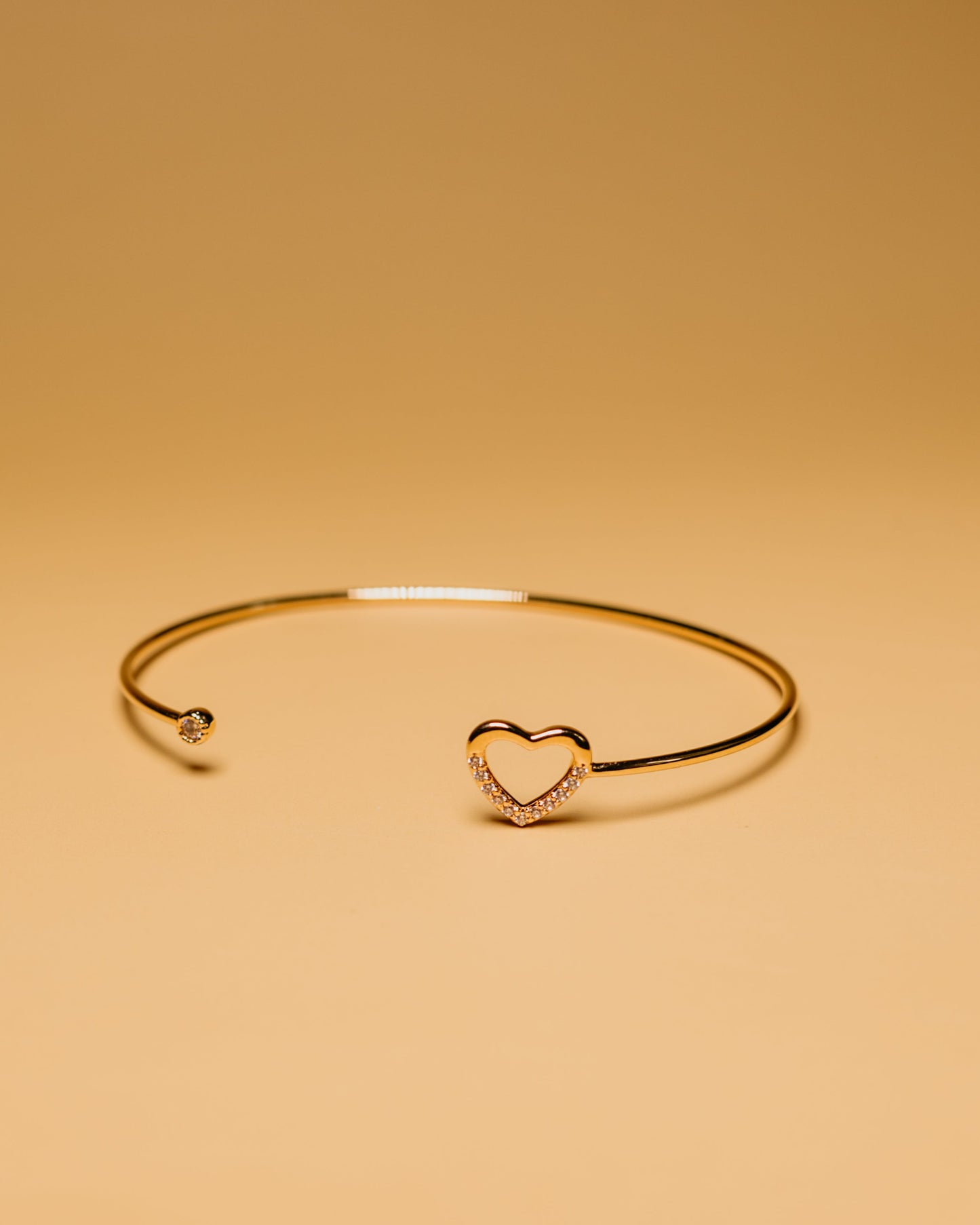 Gold bracelet with a heart-shaped clasp on a beige background