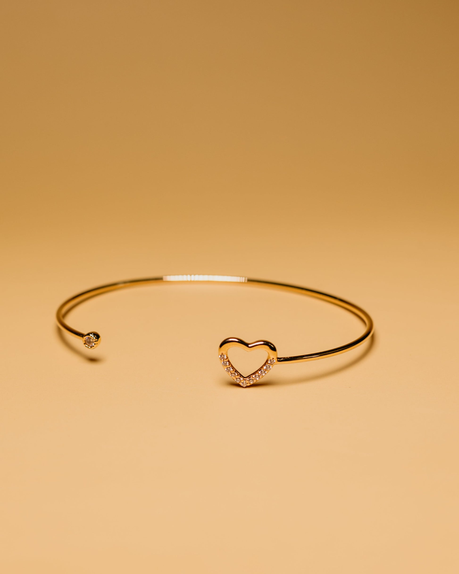 Gold bracelet with a heart-shaped clasp on a beige background