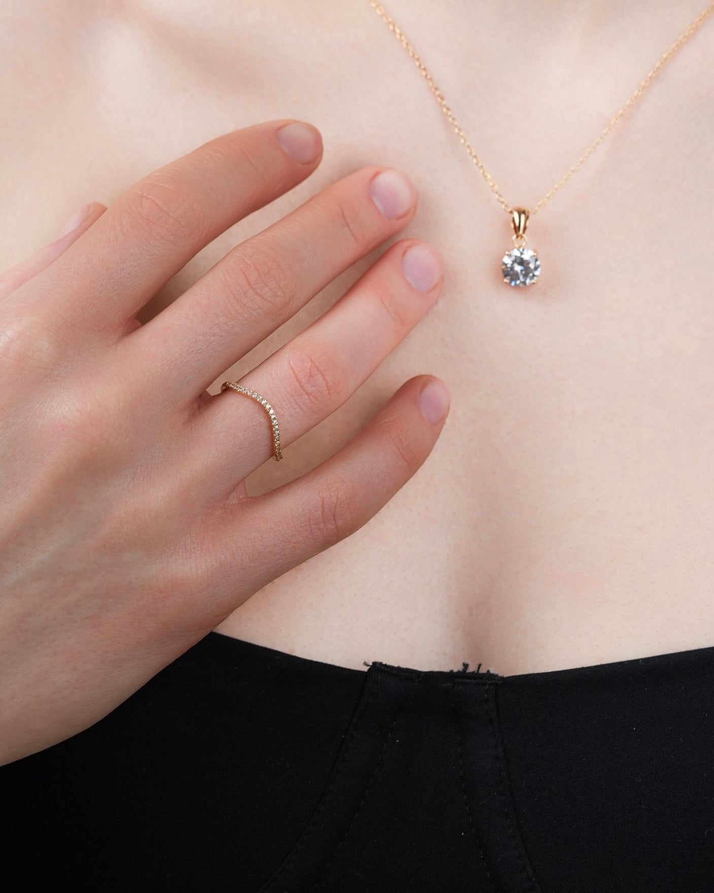 Thin 18k gold-plated band ring with cubic zirconia stones worn on a hand, paired with a solitaire necklace
