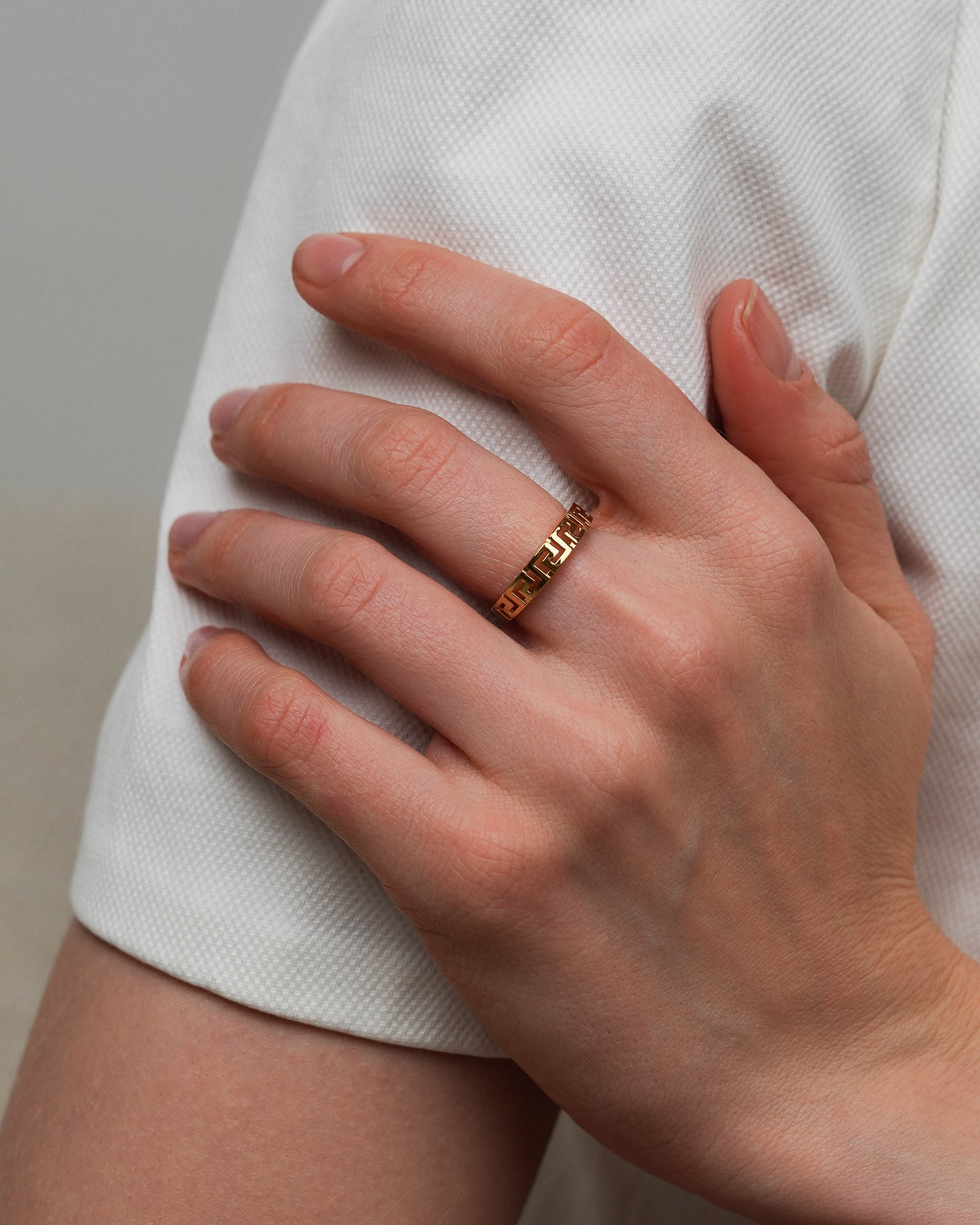 Gold plated geometric ring worn on a hand resting on a light fabric sleeve