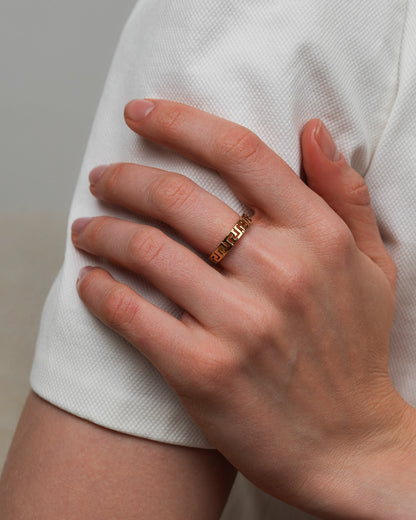 Gold plated geometric ring worn on a hand resting on a light fabric sleeve