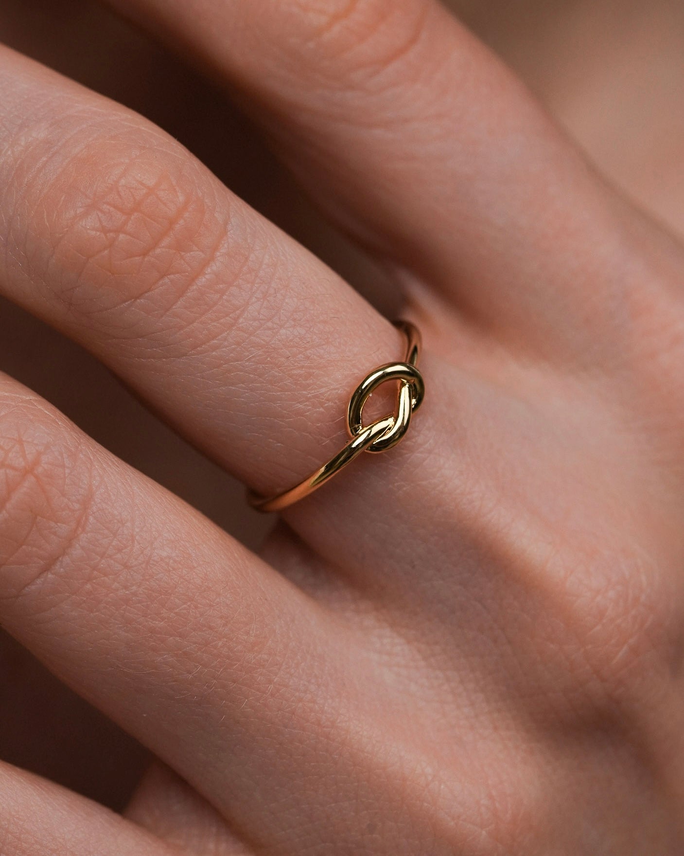 Fira gold knot ring worn on finger, 18k gold plated minimalist band ring close up