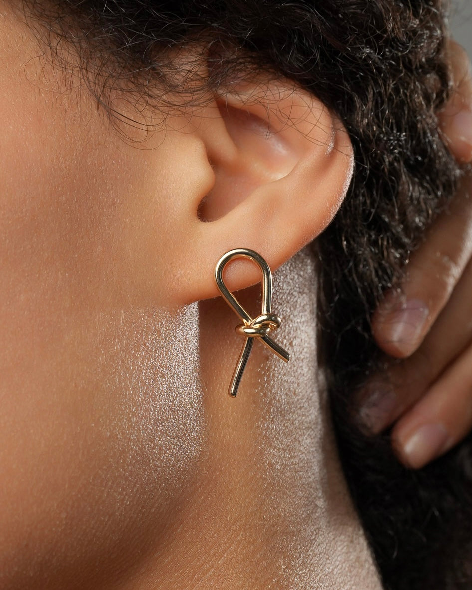 Gold knot stud earrings in 18k gold plating 3 microns worn on ear close-up