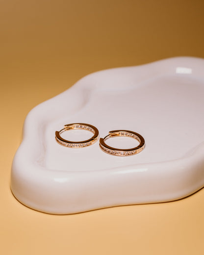Gold hoop earrings on a white ceramic dish with a beige background