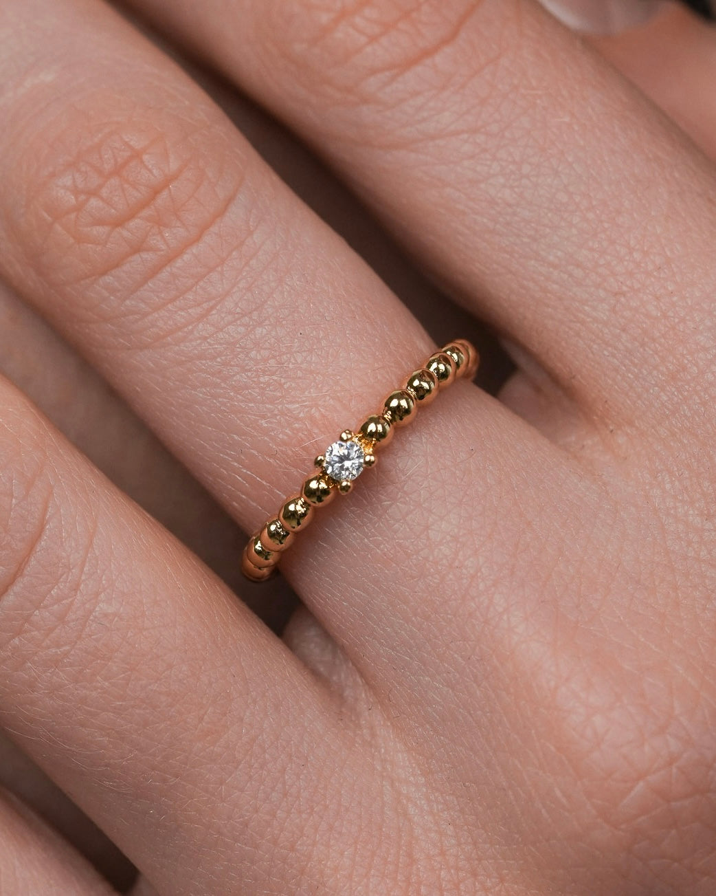 minimal gold ring with single cubic zirconia on rounded beaded band, delicate 18k gold plated ring close up
