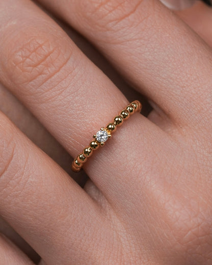 minimal gold ring with single cubic zirconia on rounded beaded band, delicate 18k gold plated ring close up
