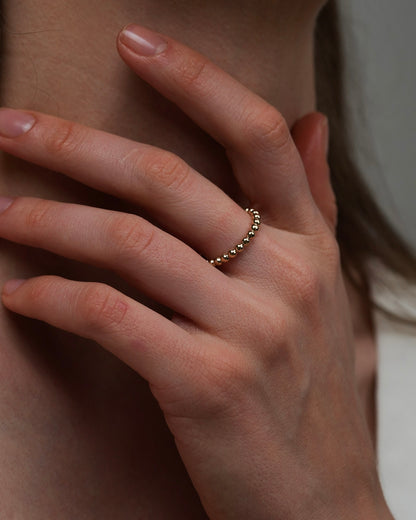 Gold-plated beaded ring worn on hand touching neck lifestyle jewelry shot