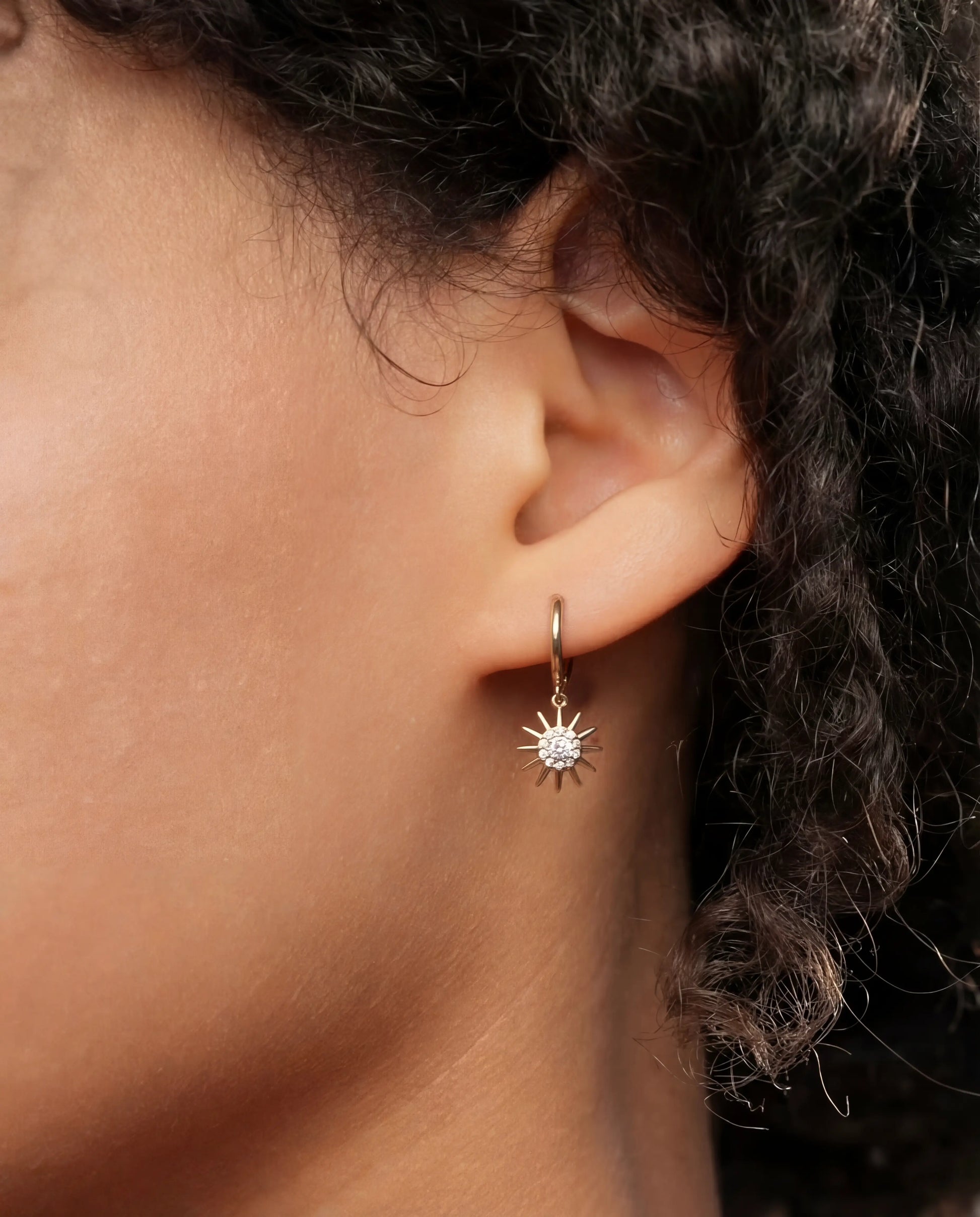Close-up of Muna gold plated hoop earring with sun charm and cubic zirconia worn on ear