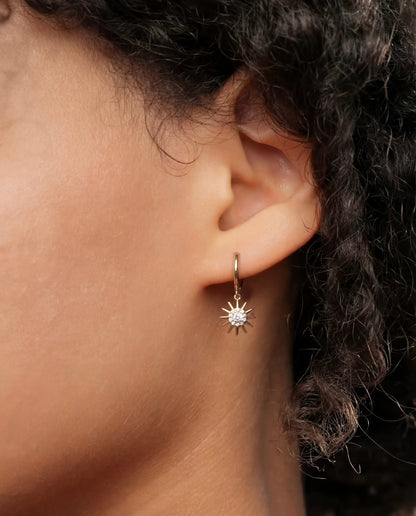 Close-up of Muna gold plated hoop earring with sun charm and cubic zirconia worn on ear