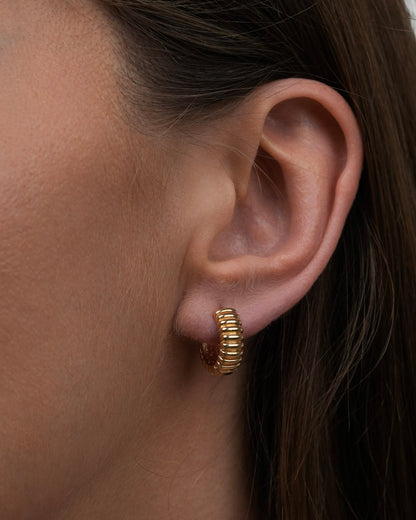 Close-up of gold plated small ribbed hoop earrings worn on ear