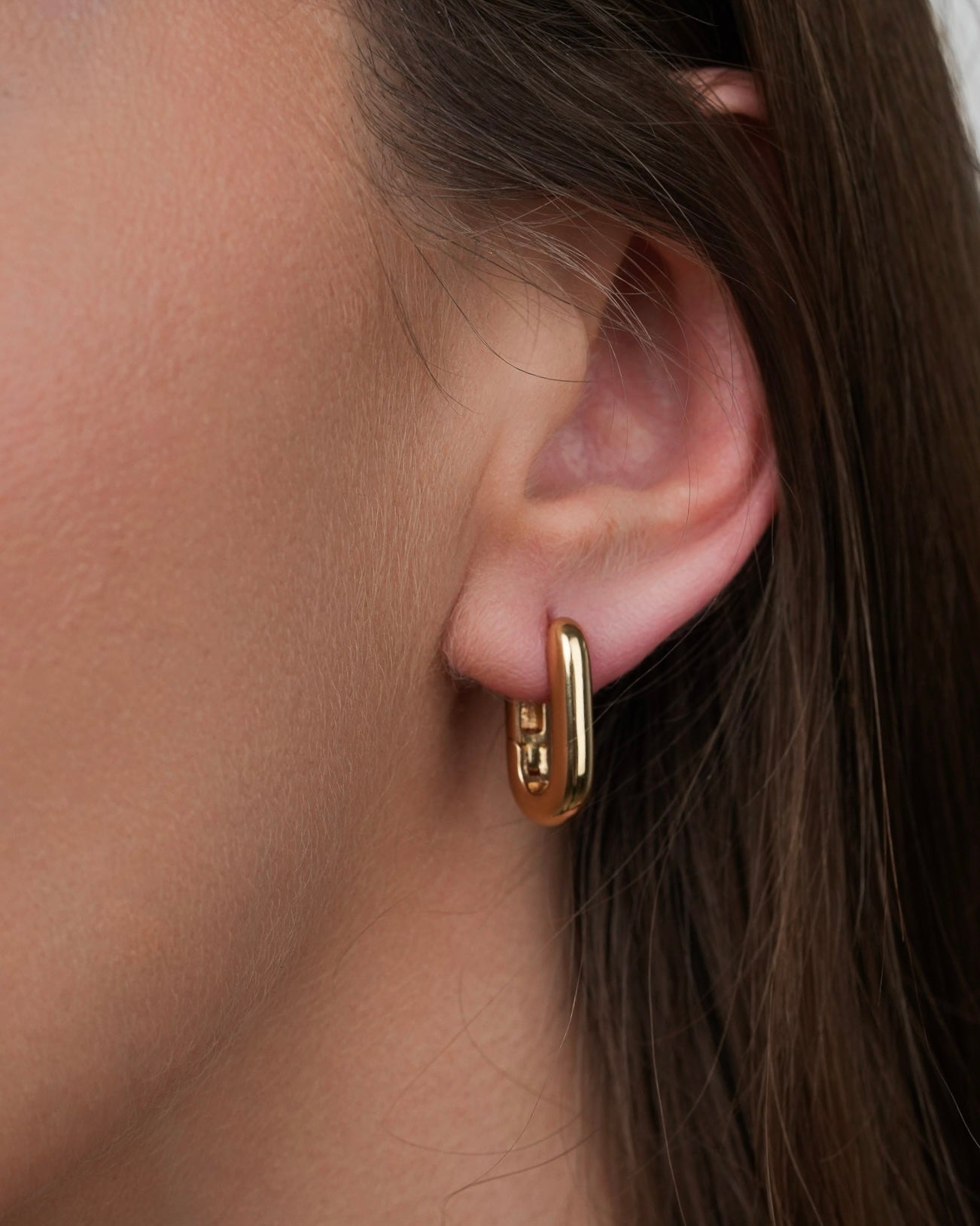 rita minimalist gold plated hoop earrings worn on ear, close-up view