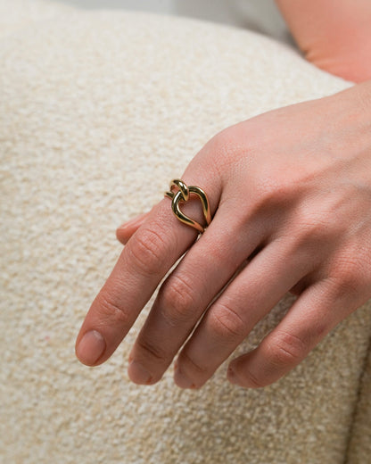 Gold-plated sculptural ring worn on hand, showing its curved intertwined form